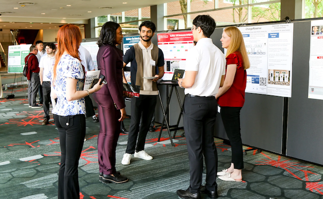 People stand in a small group discussing research posters displayed on boards during a conference poster session.