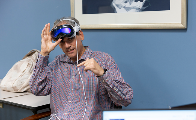 Kyle Johnsen, demonstrating, lifts a VR headset and gestures to a cord attached to it