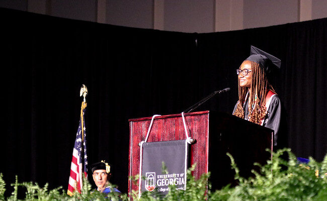 Deborah Madden smiling at the podium in her cap and gown.
