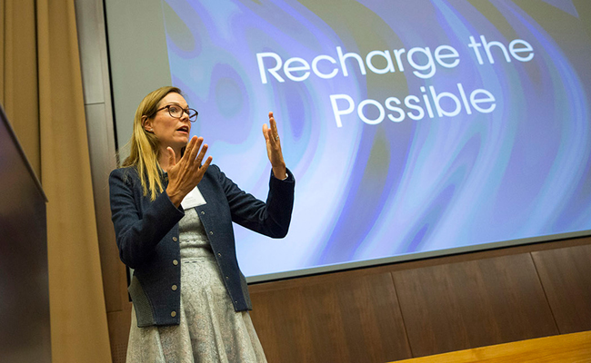 Woman speaking in front of screen that reads "recharge the possible"