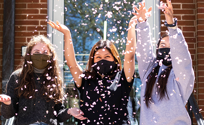 Frida Alvarado (center) and friends celebrate the arrival of Spring by tossing cherry blossoms outside the Driftmier Engineering Center.