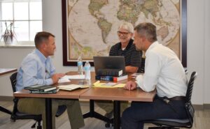 Three men sitting at a table with laptops and notebooks 