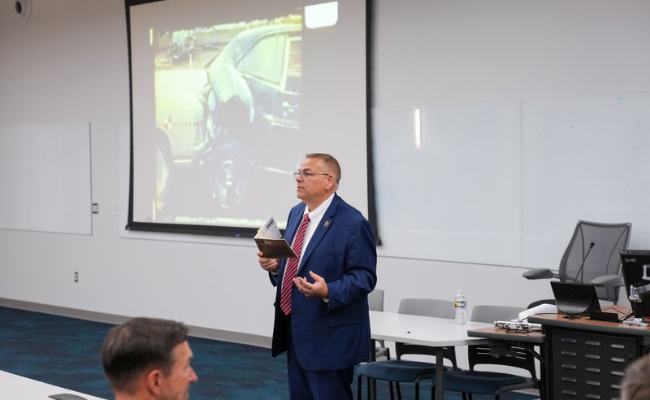 A man standing in a room and holding a book while speaking to an audience.