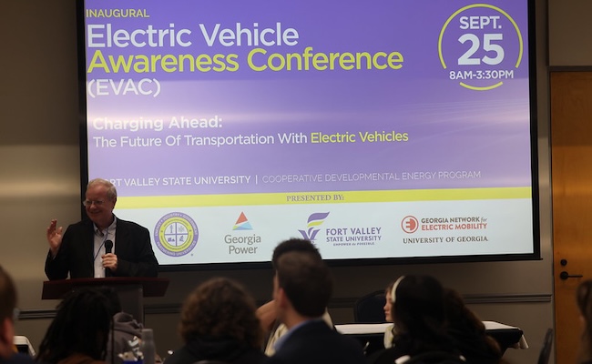 Individual standing in front of screen presenting about Electric Vehicles