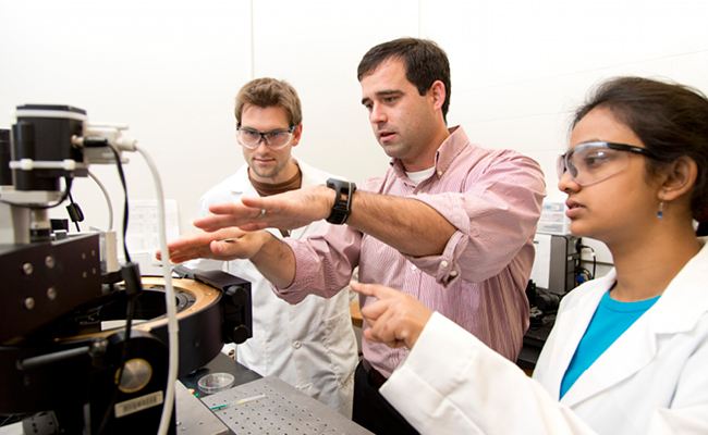 Chemistry Ph.D. student Evan White, left to right, talks with professor Jason Locklin and fellow Chemistry Ph.D. student Anandi Roy about an experiment on a multiskop surface analytical instrument in Locklin's labs at the Riverbend Research South facility.