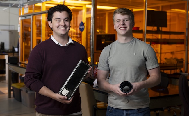 4th year undergraduate and principal investigator Grant Baumann holds a small satellite along with 4th year undergraduate and chief engineer Ben Pumphrey as he holds the net deployment mechanism for the satellite their are creating with their company Skyfall Space Inc. Their satellite will be about twice the size of the one Grant is holding and while they originally met in the Small Satellite Lab where they are pictured, the Skyfall Space debris catcher is an independent project from the lab.