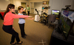 Sun Joo "Grace" Ahn, left, helps nine-year-old Maddie Lacey of Watkinsville interact with the virtual buddy fitness kiosk in the Games and Virtual Environments Lab at Grady College of Journalism and Mass Communication, while Maddie's mother, Cara Lacey, looks on.